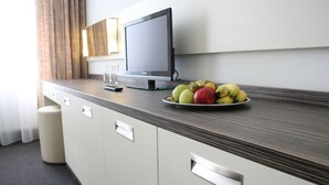 A hotel room with a flat-screen TV, a fruit plate on the counter, and a trash bin. - Hotel Malta (Karlovy Vary)