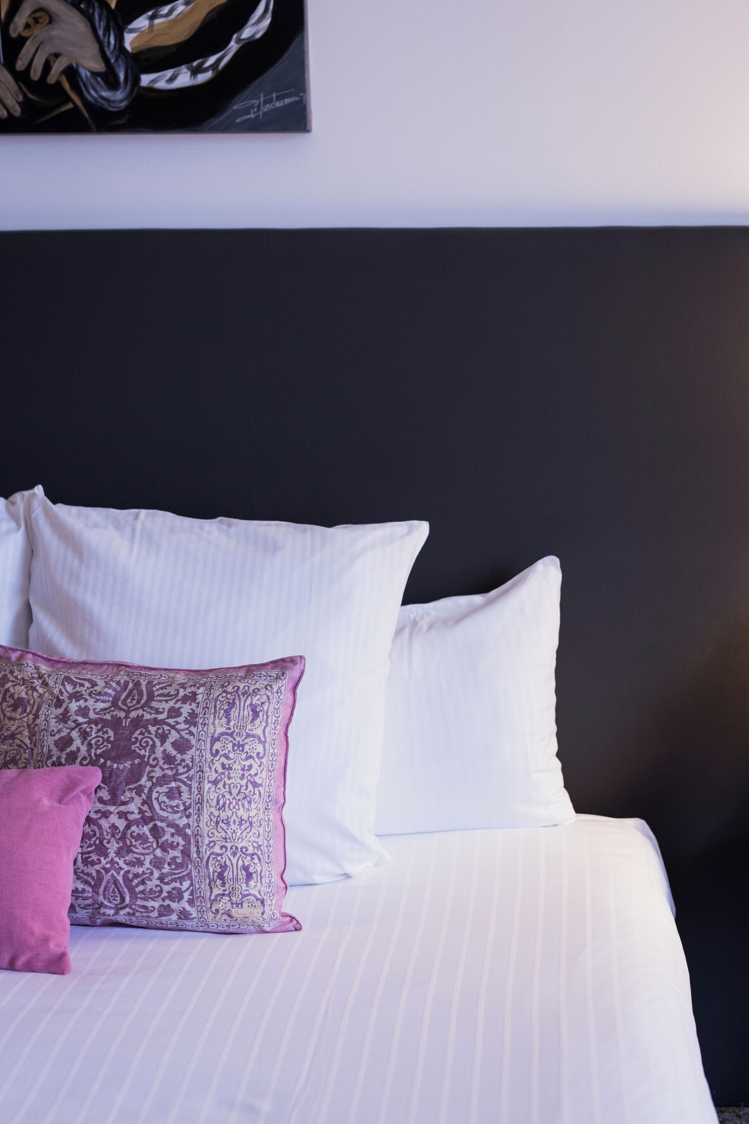 Una cama con sábanas blancas y una única almohada estampada.