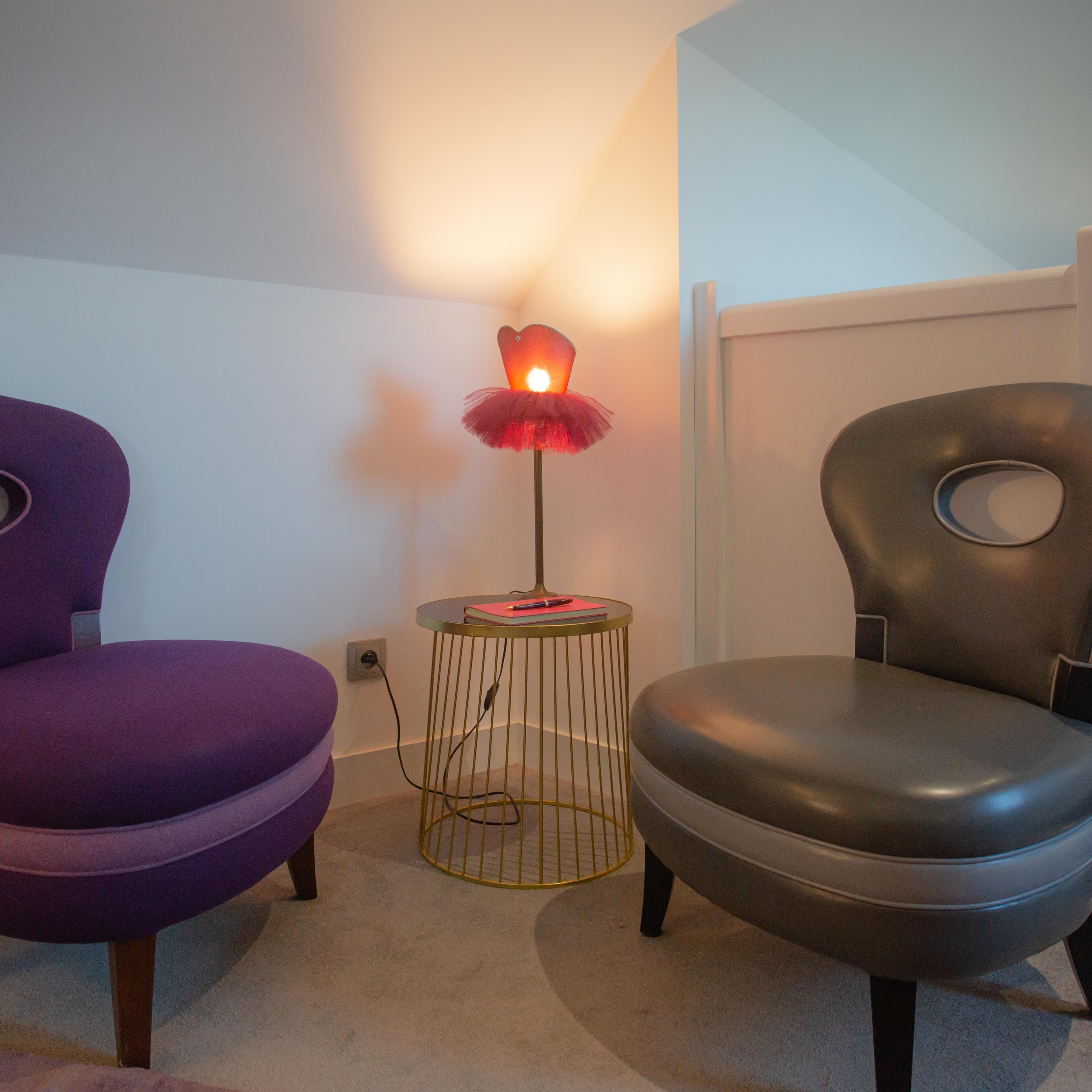 A room with two chairs, one purple and one black, and a small table with a lamp.