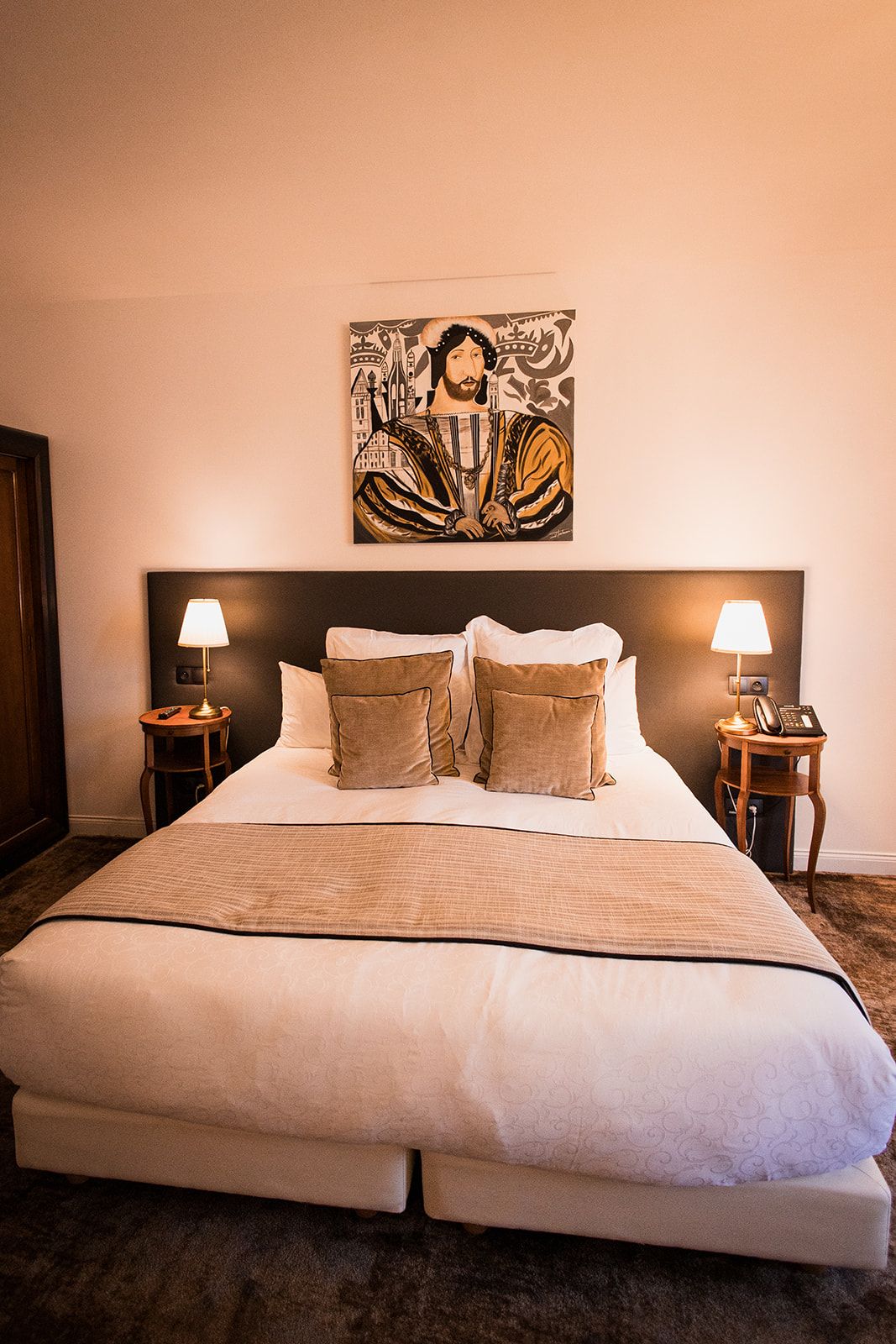 A hotel room with a large bed, two bedside tables with lamps, a painting on the wall, and a carpeted floor.