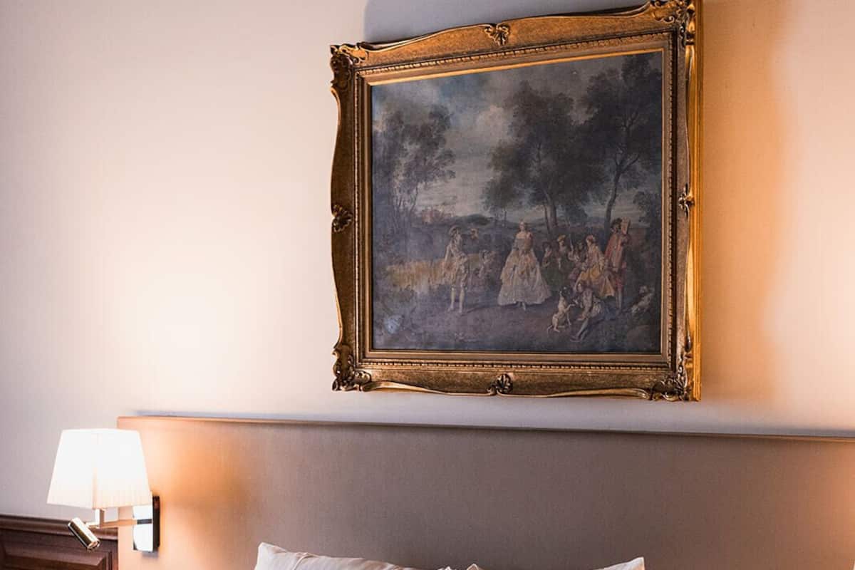 A hotel room with a bed, a painting on the wall, a nightstand, and a lamp.
