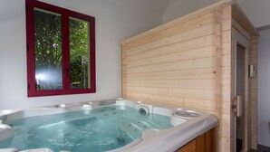 Une cabane en bois dotée d’un bain à remous, d’une fenêtre aux cadres rouges et d’une porte donnant sur un espace douche.