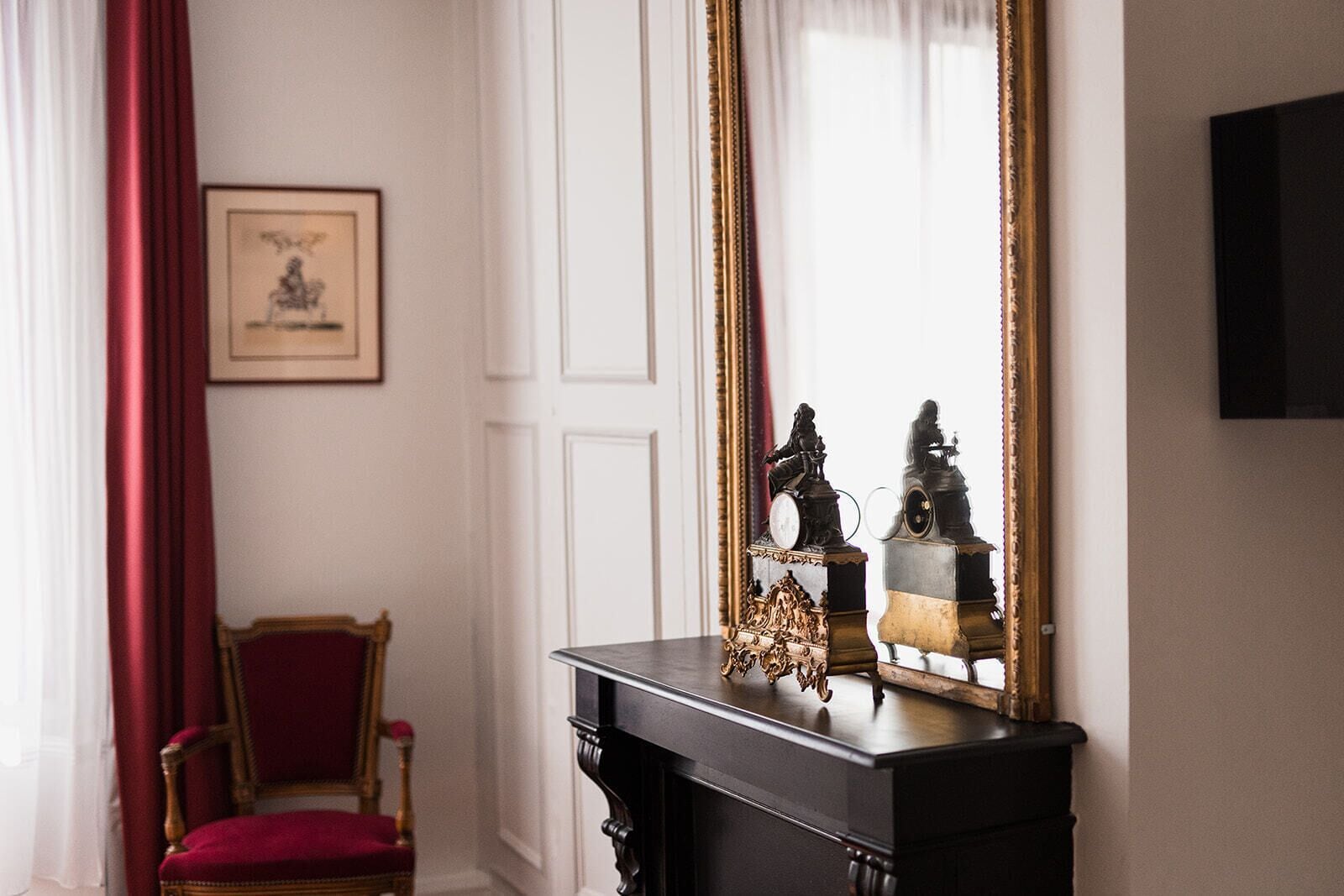 Een kamer met een grote spiegel, een rode stoel en een foto in een lijst aan de muur.