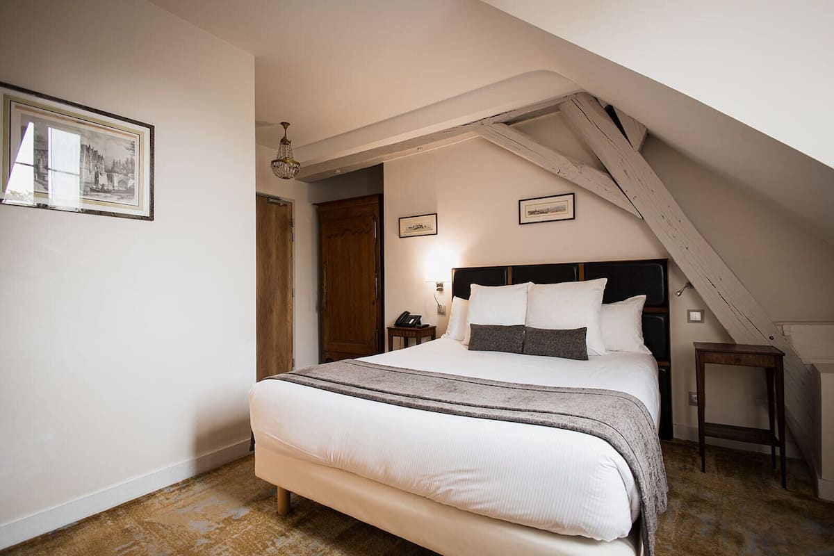 A bedroom with a large bed, a wooden door, a nightstand, and a chandelier.