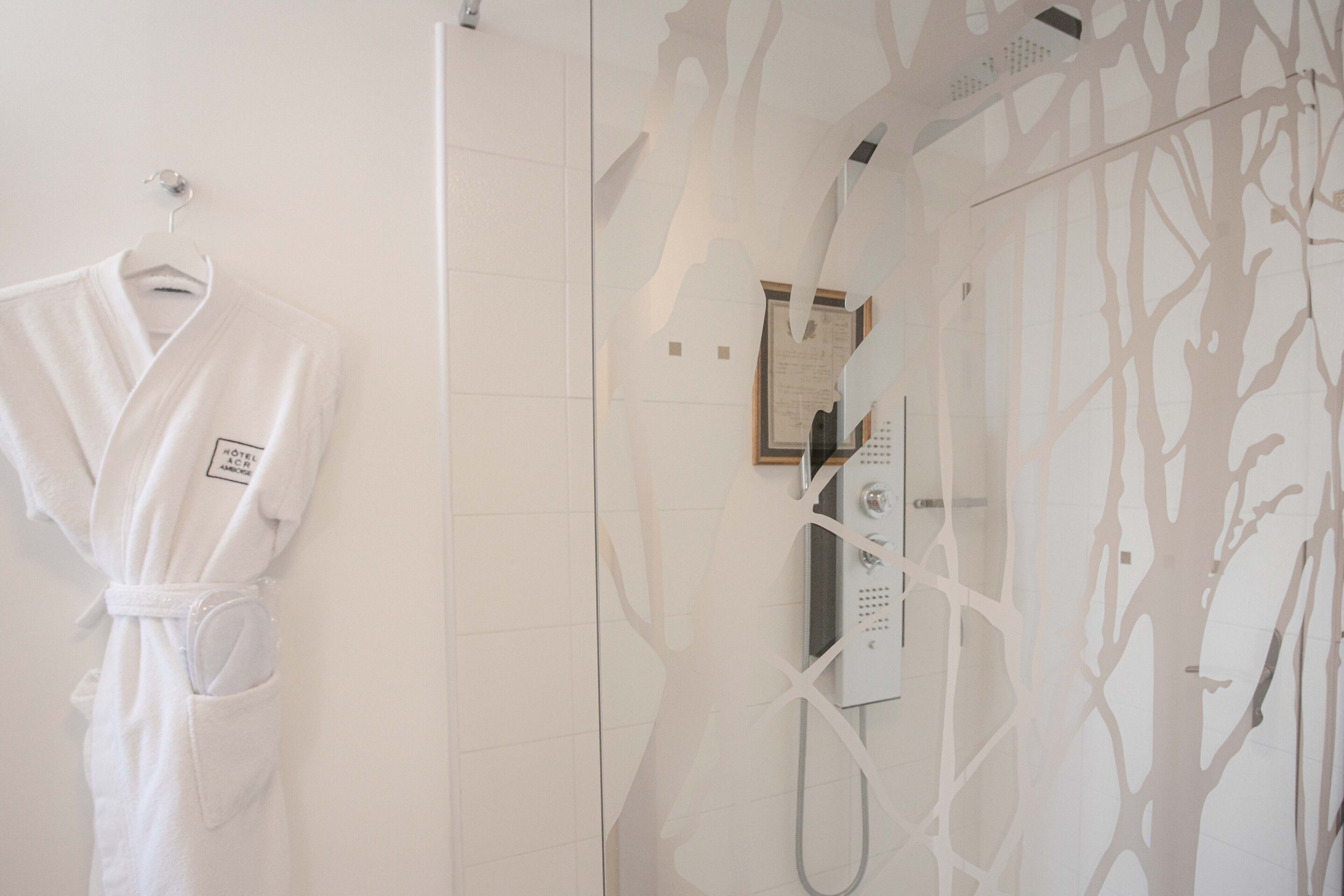 Un baño con cabina de ducha de vidrio, una bata blanca colgada en un perchero y una pared con diseño de árbol.