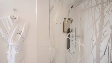 Un baño con cabina de ducha de vidrio, una bata blanca colgada en un perchero y una pared con diseño de árbol.