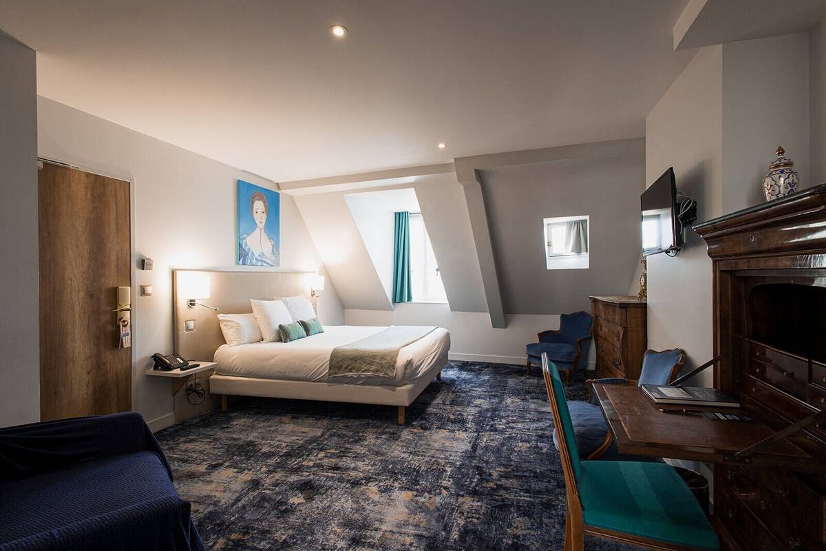 A hotel room with a bed, desk, chair, and a television.