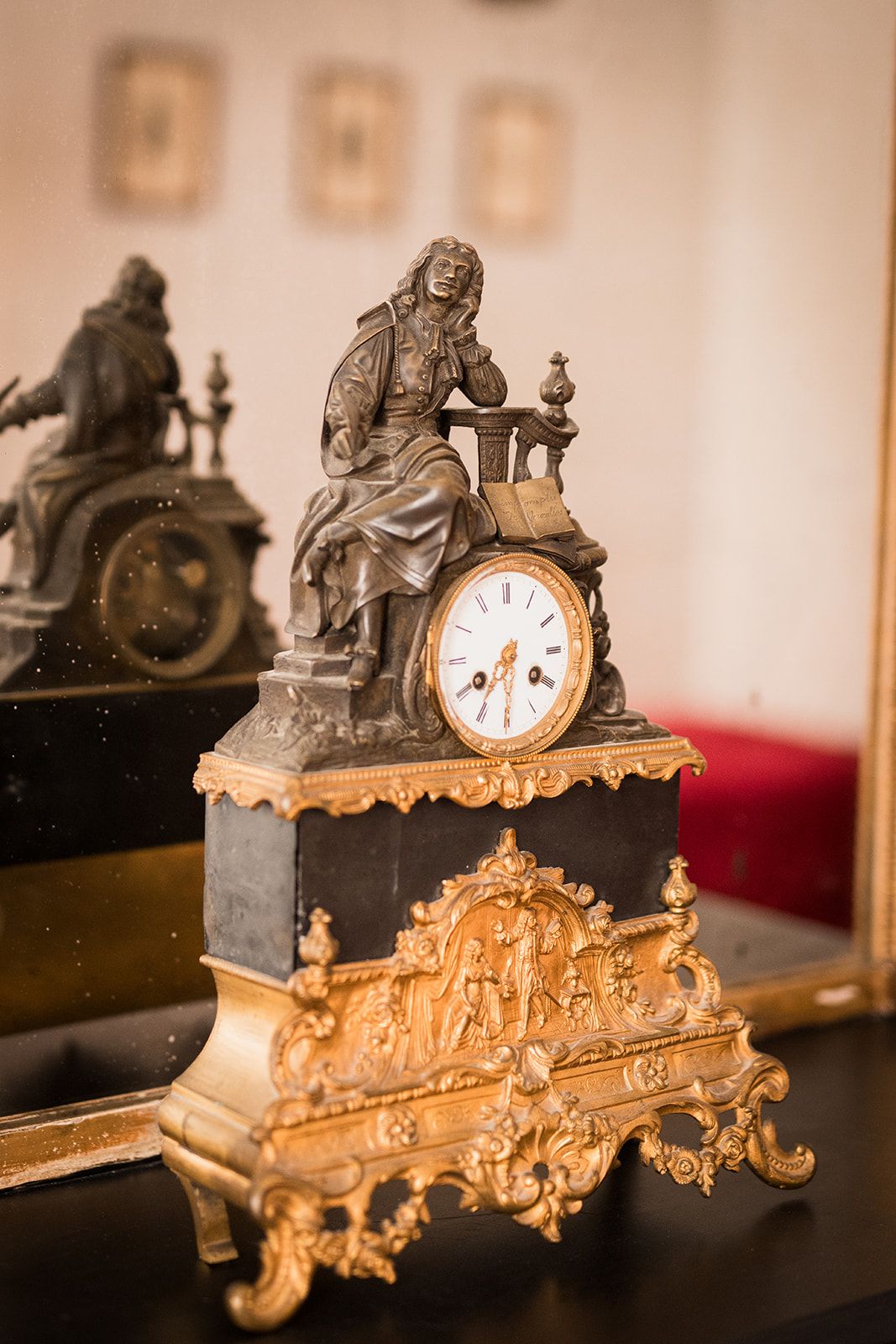 Une horloge détaillée, surmontée d’une statue, placée sur un fond sombre avec un coussin rouge.