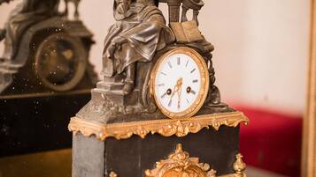 Une horloge détaillée, surmontée d’une statue, placée sur un fond sombre avec un coussin rouge.