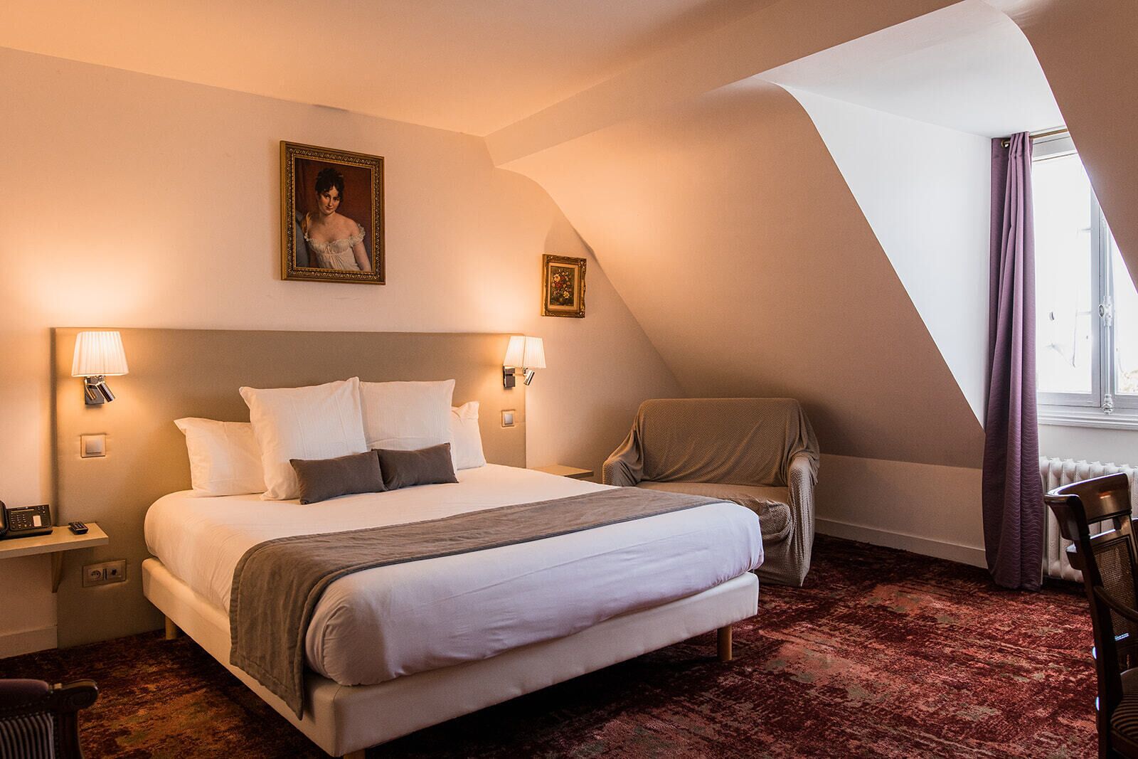 A hotel room with a large bed, two bedside lamps, a chair, a window with curtains, and a painting on the wall.