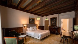 Une chambre d’hôtel avec un grand lit, deux tables de chevet, un bureau, une chaise et une porte donnant sur une autre pièce.