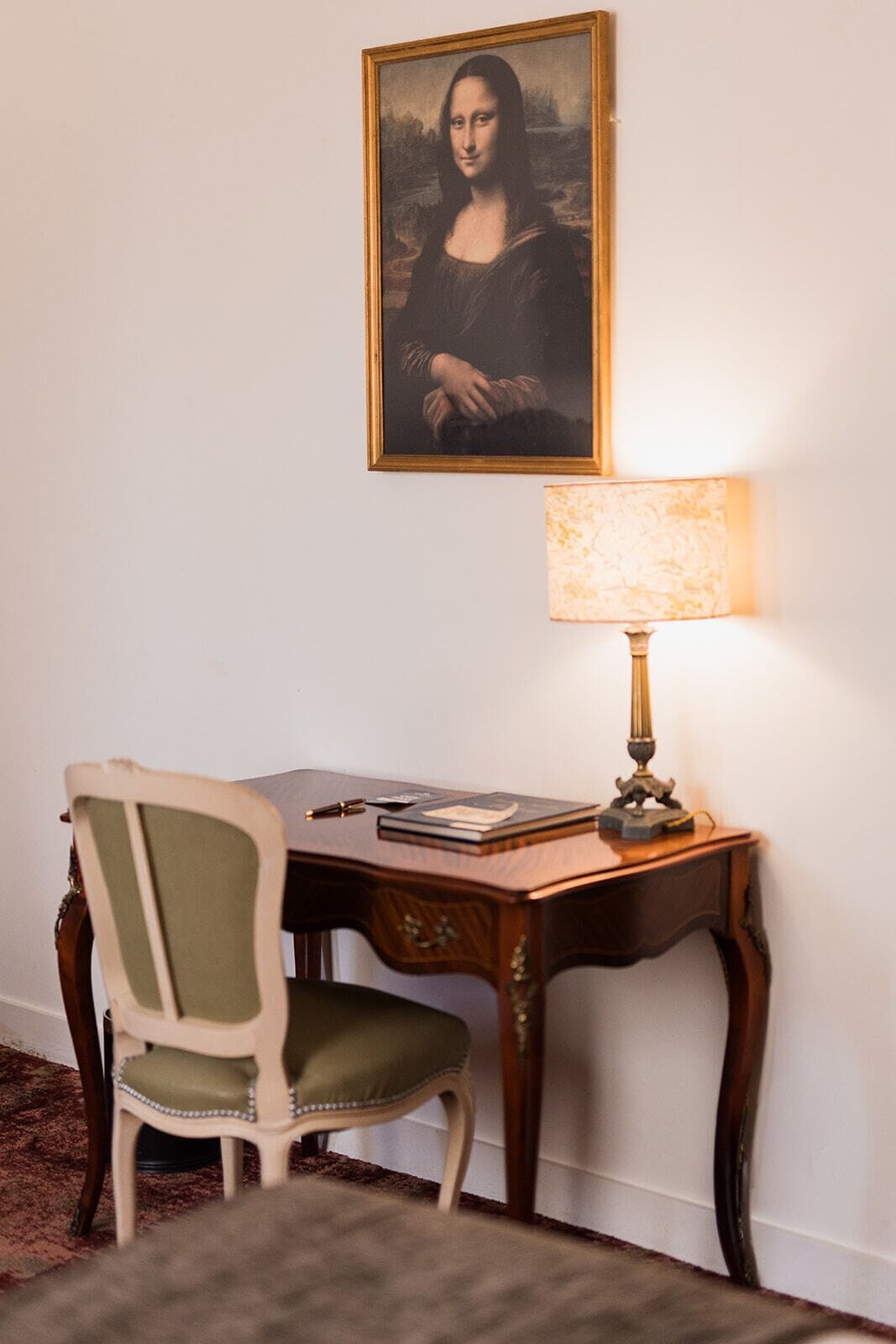 A desk with a lamp, a chair, and a framed artwork on the wall.