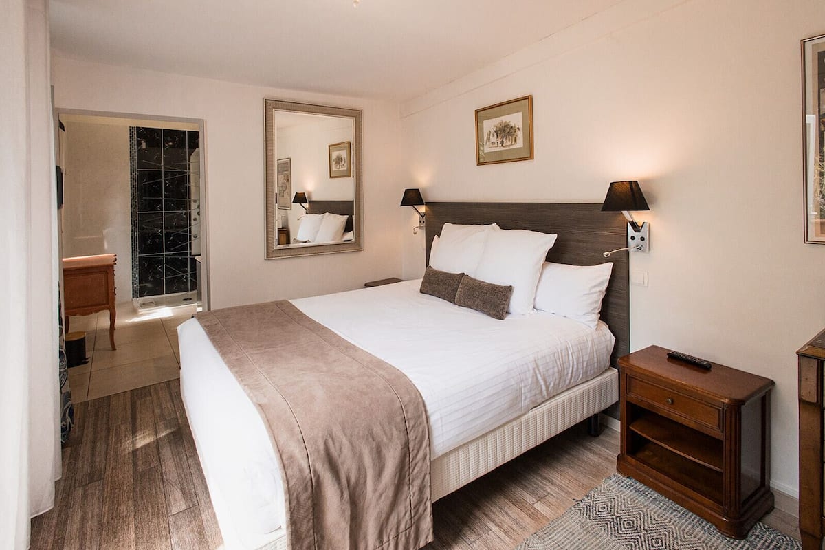 A neatly arranged bedroom with a large bed, bedside tables, a mirror, and a framed picture on the wall.