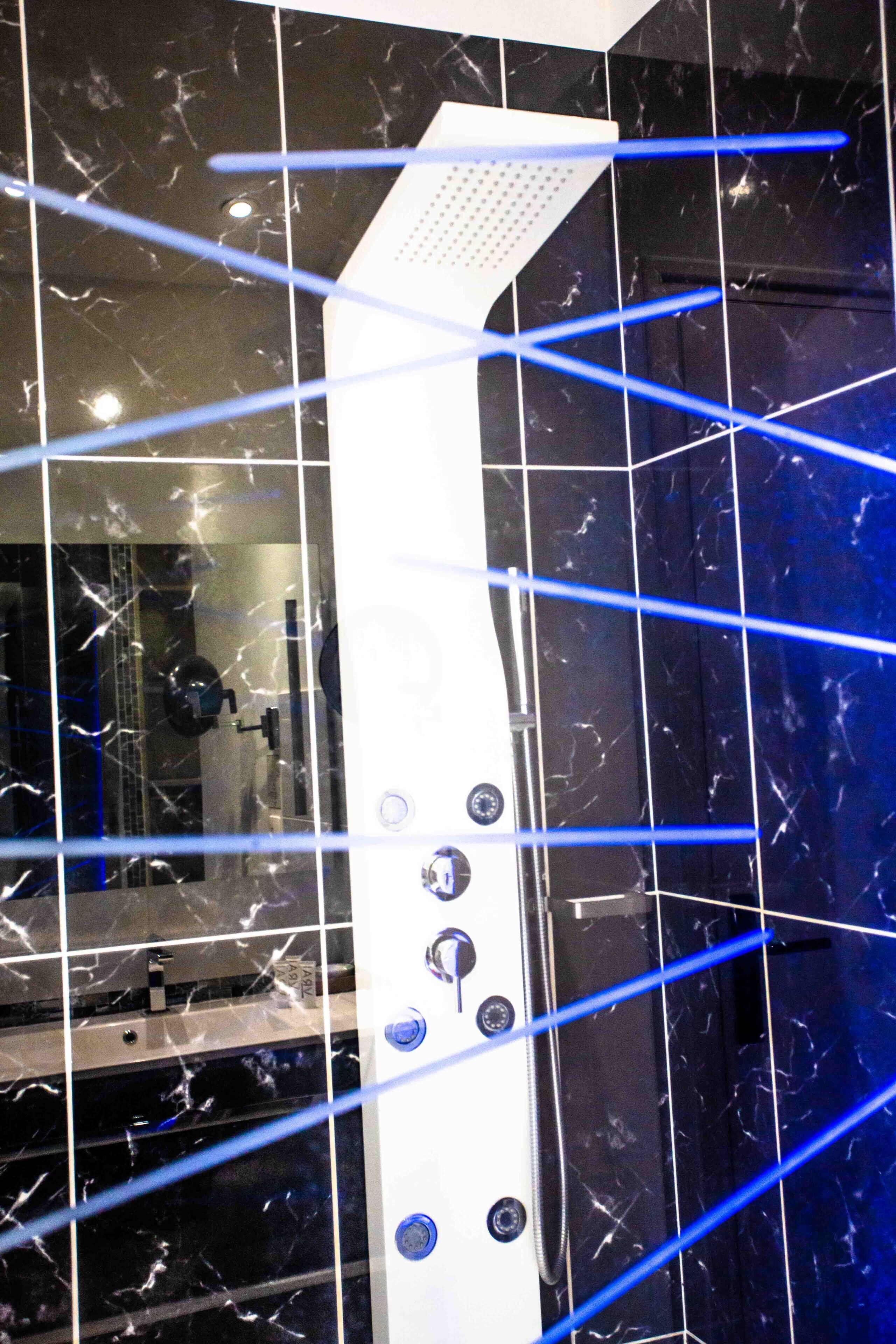 A bathroom with a white shower enclosure, black marble tiles, and a visible water control panel.