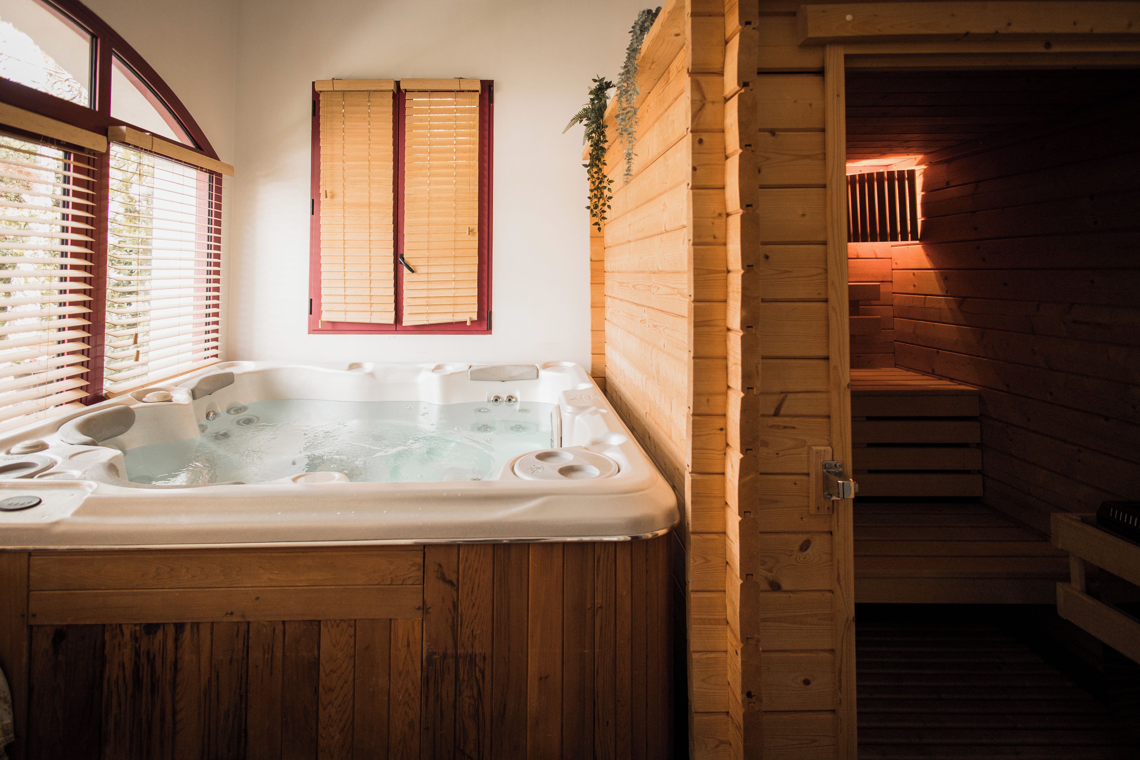 A wooden cabin with a hot tub, wooden walls, and a window with blinds.
