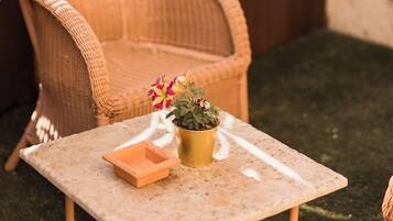 Une chaise en osier, une petite table avec un pot de fleurs et un jardinier.