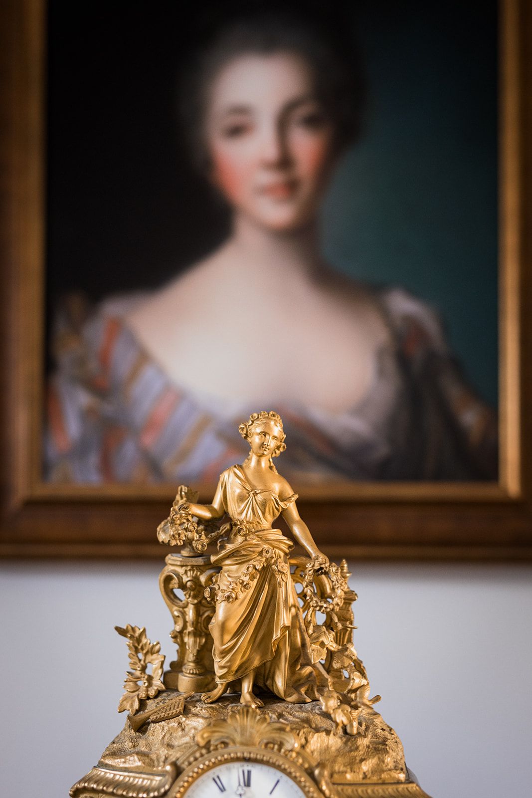 Een gouden beeld op een klokvoet, met een schilderij op de achtergrond.