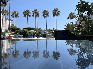 Una piscina al aire libre, sombrillas, sillones reclinables de piscina