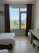 Quarto de hotel com cama, escrivaninha e vista para a praia e o oceano.