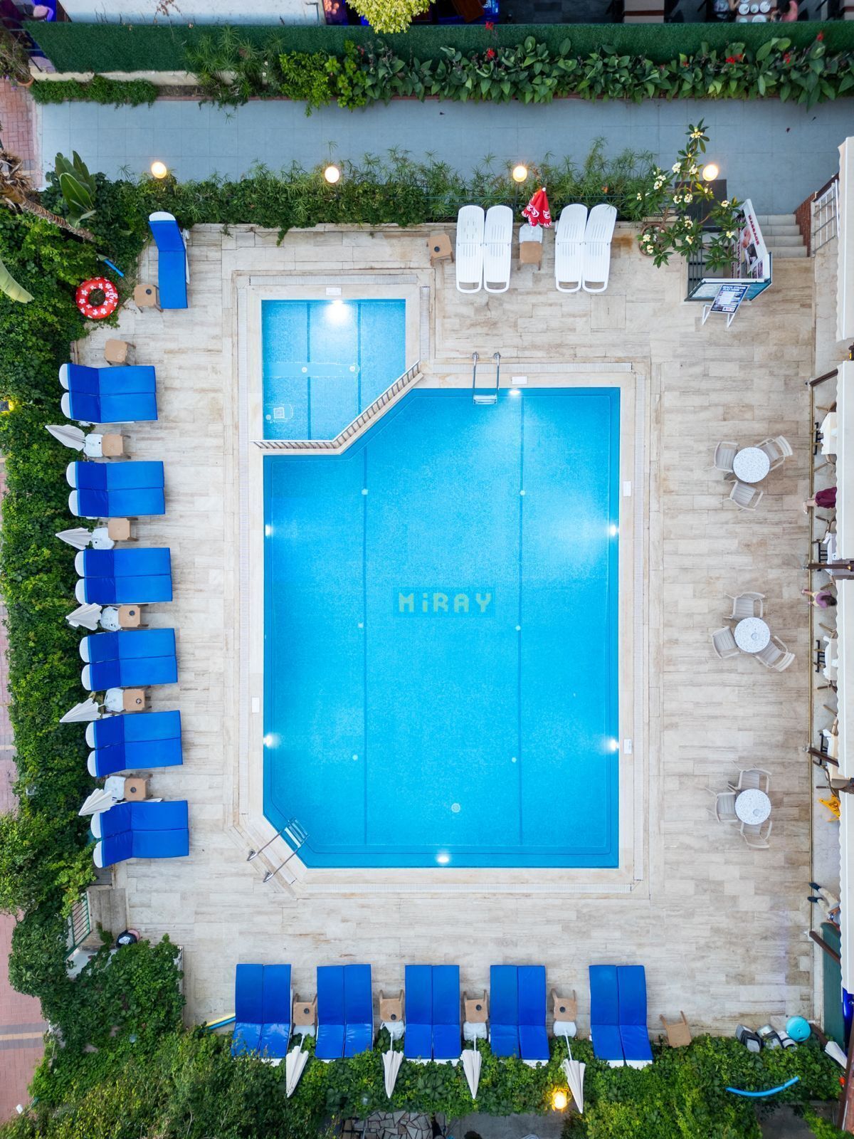 A rooftop swimming pool with a blue interior, surrounded by blue lounge chairs and white sun loungers.
