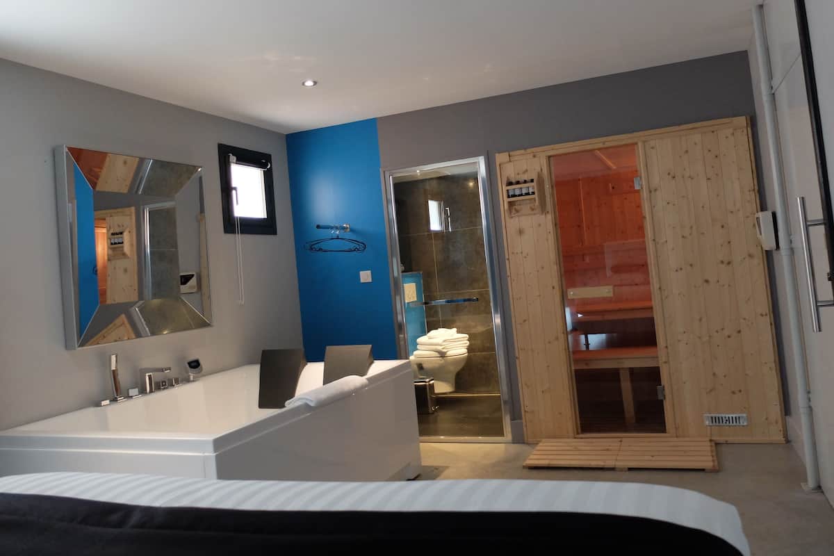A modern bathroom with a large bathtub, a mirror, and a wooden sauna door.