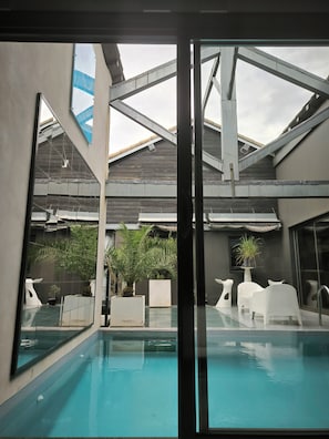 A modern indoor pool area with clear glass walls, a pool, and white lounge chairs.