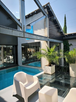 A modern outdoor pool area with glass flooring, white lounge chairs, and potted plants.