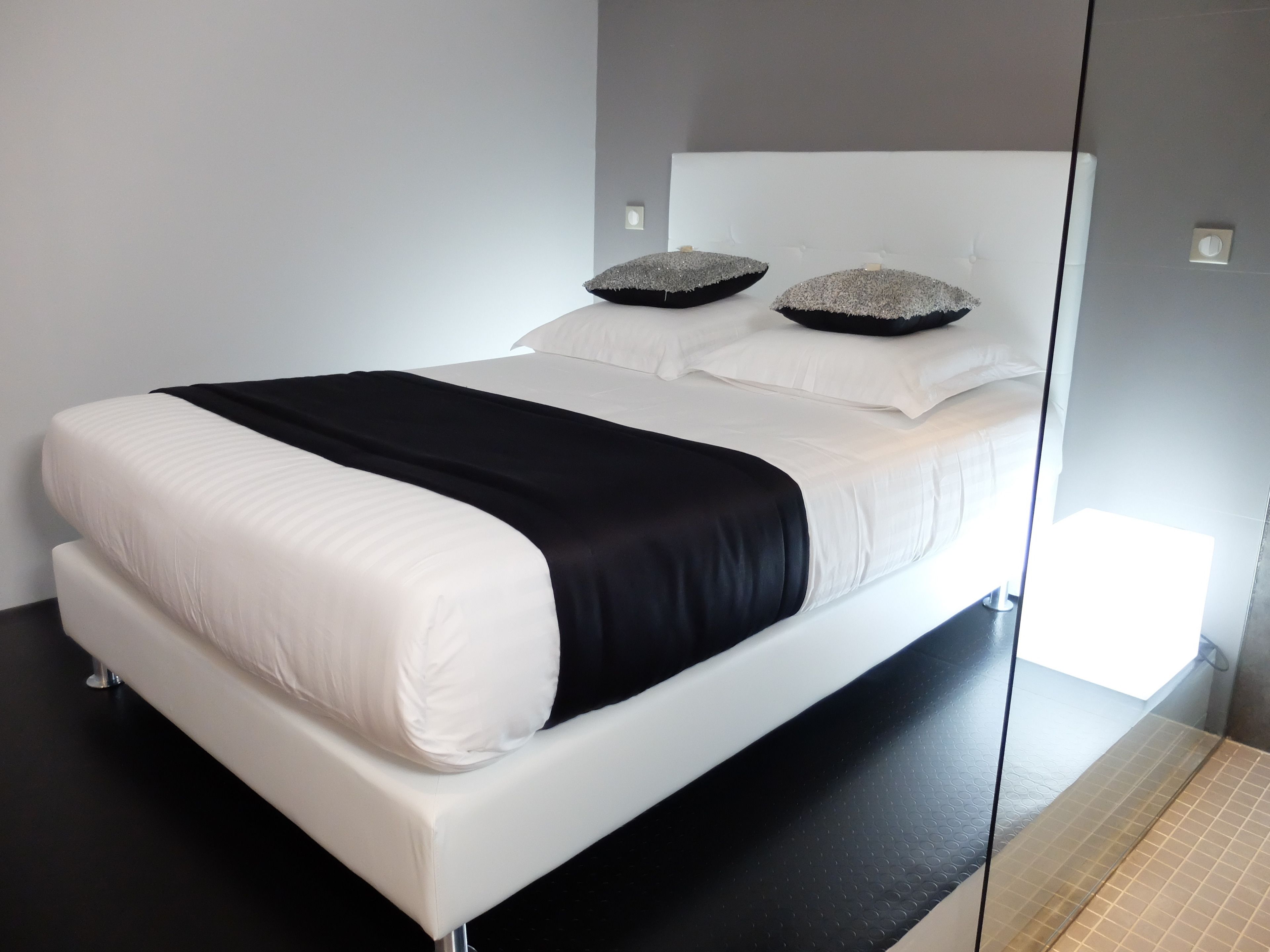 Ein modernes Schlafzimmer mit einem weißen Bett, schwarz-weiß gestreifter Bettwäsche und zwei Zierkissen.