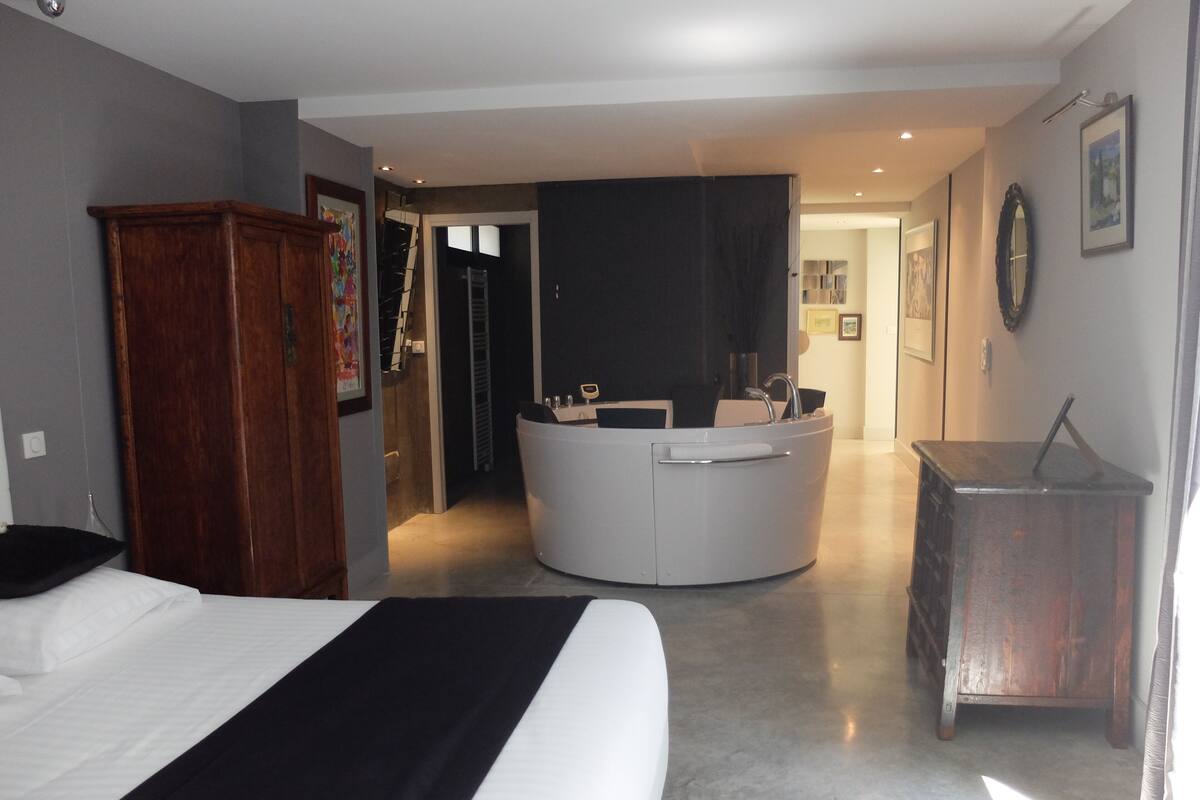 A modern hotel room with a large bed, a round bathroom, and a wooden dresser.