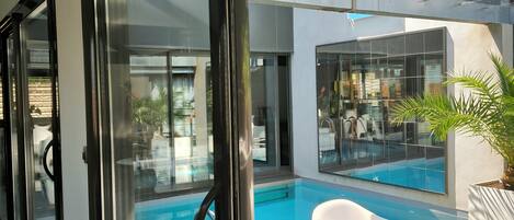 A modern indoor pool area with glass walls, a clear view of the pool, and white lounge chairs.