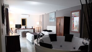 A modern hotel room with a large bathtub, a bed with white linens, a desk with a flat-screen TV, and a dining area with a table and chairs. - Be Loft B&B Pool & Spa (Avignon)