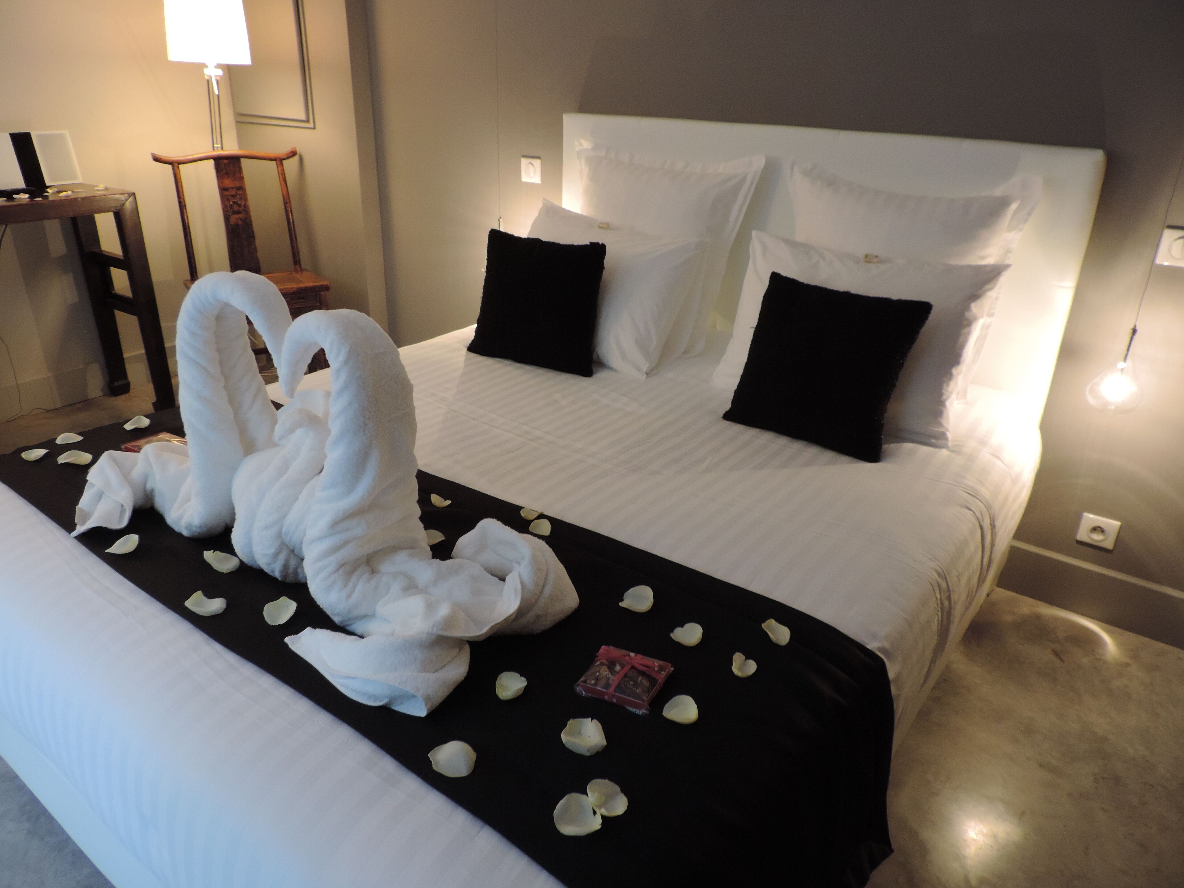 Une chambre d’hôtel avec un lit parfaitement fait, une serviette en forme de cygne et des pétales de rose sur le lit.