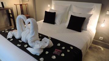 Une chambre d’hôtel avec un lit parfaitement fait, une serviette en forme de cygne et des pétales de rose sur le lit.