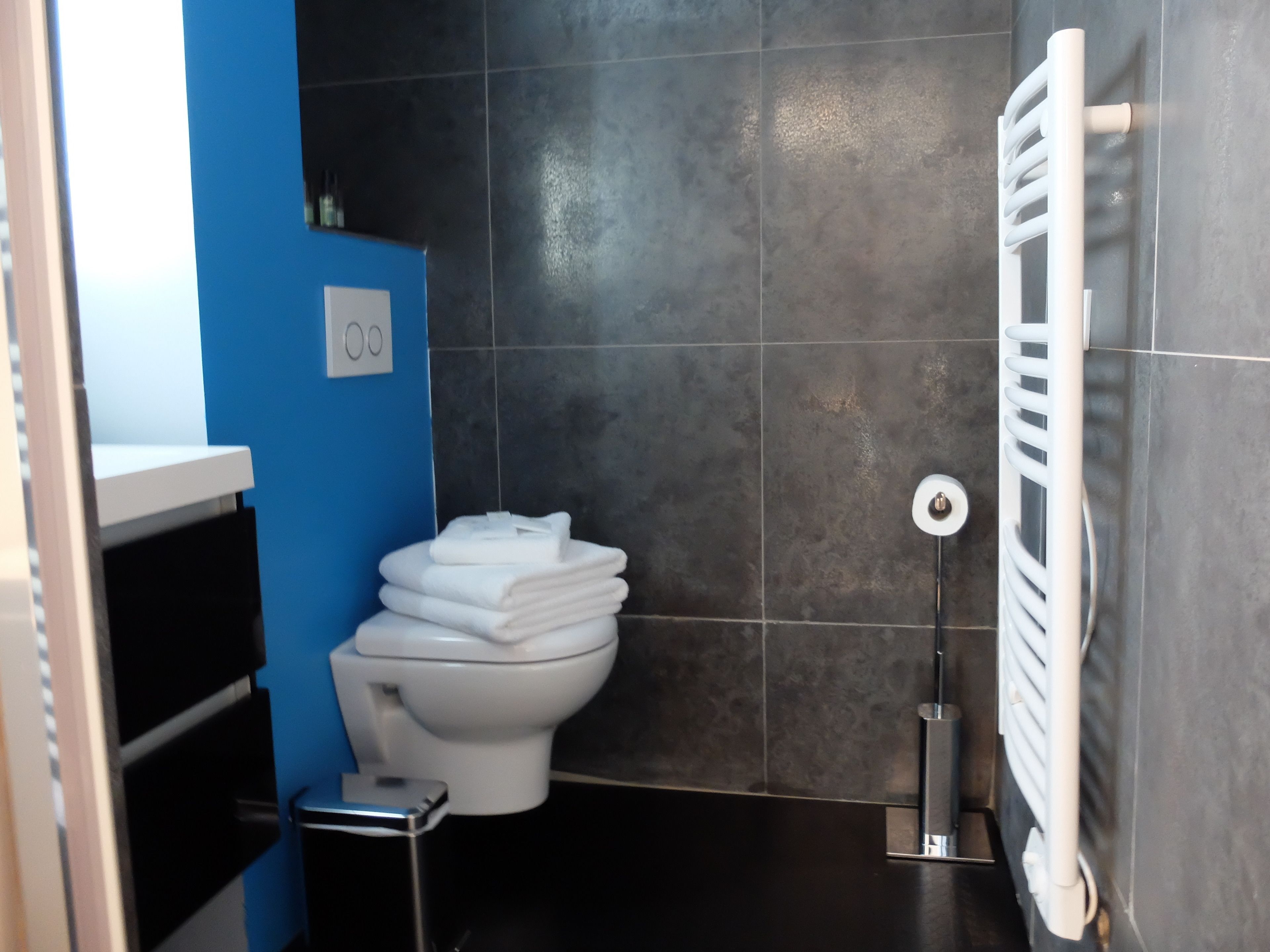 A bathroom with a toilet, a stack of white towels, a radiator, and a blue wall.