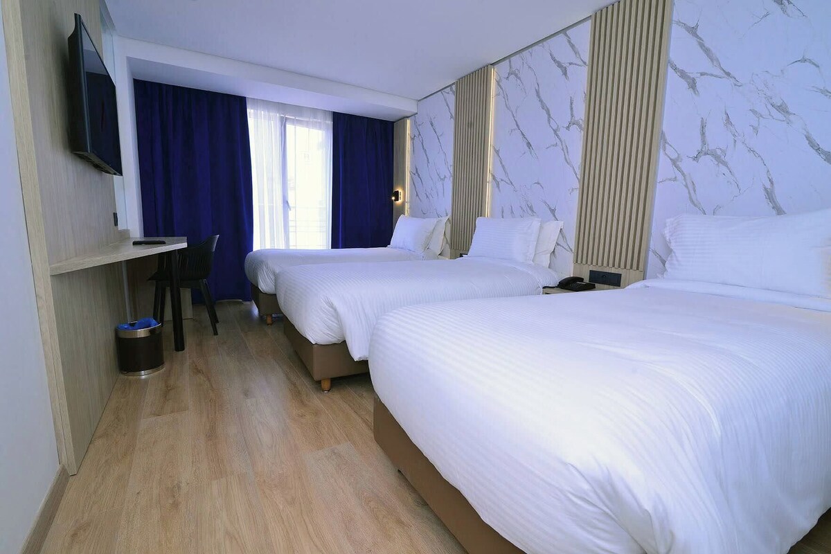 A hotel room with two beds, a desk, a TV, and a window with curtains.