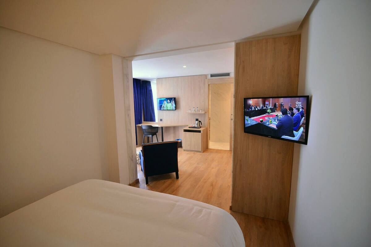 Habitación de hotel con cama, televisión montada en la pared, escritorio con silla y una pequeña zona de kitchenette.