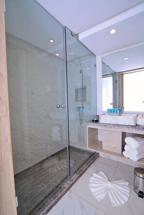 A modern bathroom with a glass-enclosed shower, marble tiles, a vanity with a mirror, and a large window.