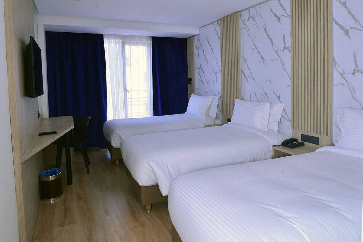 Habitación de hotel con dos camas, un escritorio, una silla, un televisor y una ventana con cortinas.
