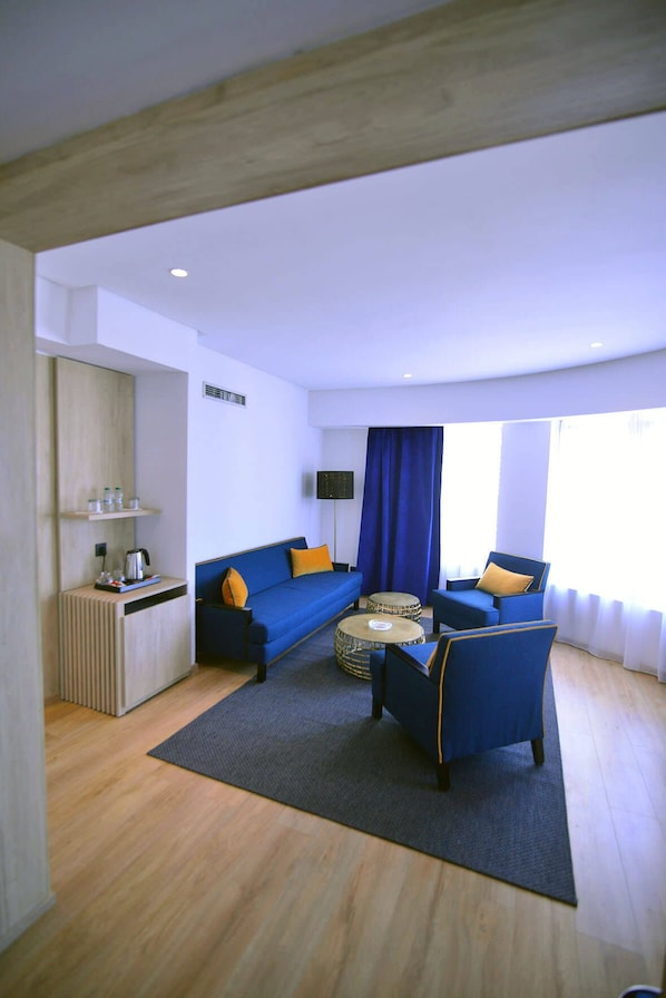 Una habitación moderna con un sofá azul, dos sillones, una mesita de café y una mesita auxiliar con un hervidor.
