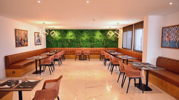 A modern dining area with booths and tables, a green wall, and artwork on the walls. - Rihab Hotel (Rabat)