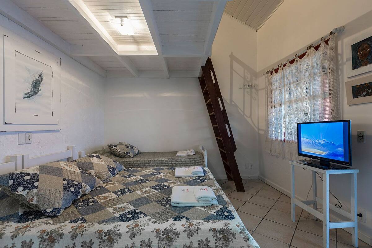 Ein Schlafzimmer mit Bett, Fernseher, einer Leiter und einem Fenster mit Vorhängen.