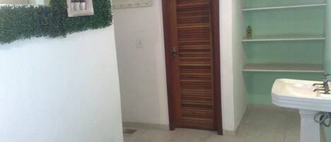 A bathroom with a wooden door, a white sink, and a green shelf unit.