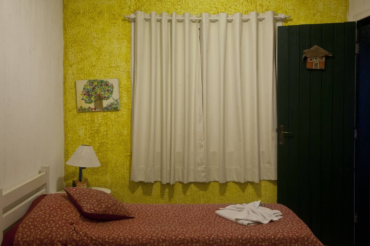 Ein Zimmer mit einem Bett, einer Lampe, einer grünen Tür und einer gelben Wand mit Struktur.