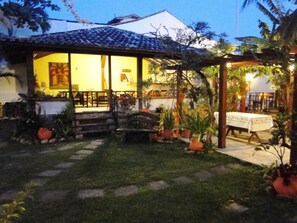 A house with a tiled roof, a porch with chairs, and a garden with potted plants. - Pousada Chez Nice (Búzios)
