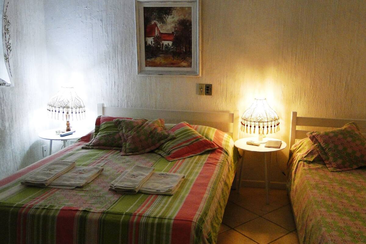 Ein Zimmer mit zwei Betten, beide mit gestreifter Bettdecke und Kissen. Zwei Nachttische mit Lampen stehen bereit. Über dem Bett links ist ein Gemälde zu sehen.