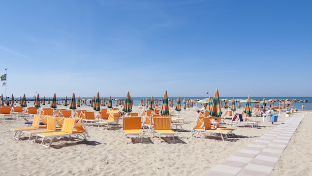 A beach with rows of orange lounge chairs and colorful umbrellas. - Hotel Cormoran (Cattolica)