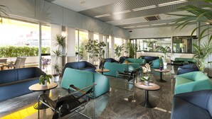 A modern lounge area with teal sofas, black metal chairs, and small tables. - Hotel Cormoran (Cattolica)