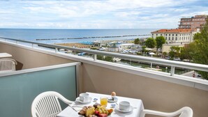 A balcony with a table set for breakfast, overlooking a beach and cityscape. - Hotel Cormoran (Cattolica)
