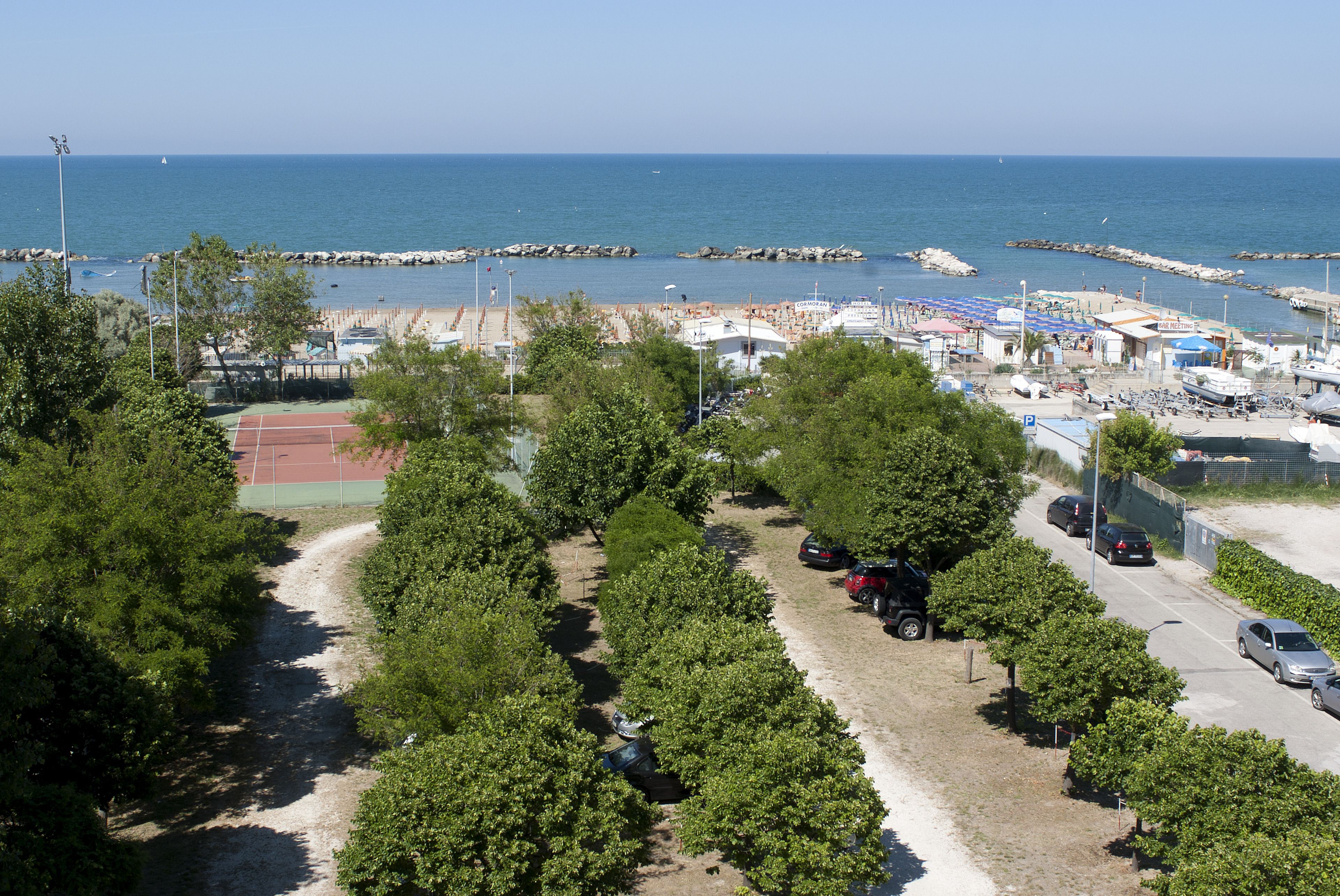 A coastal area with a beach, a tennis court, and a parking lot with cars.