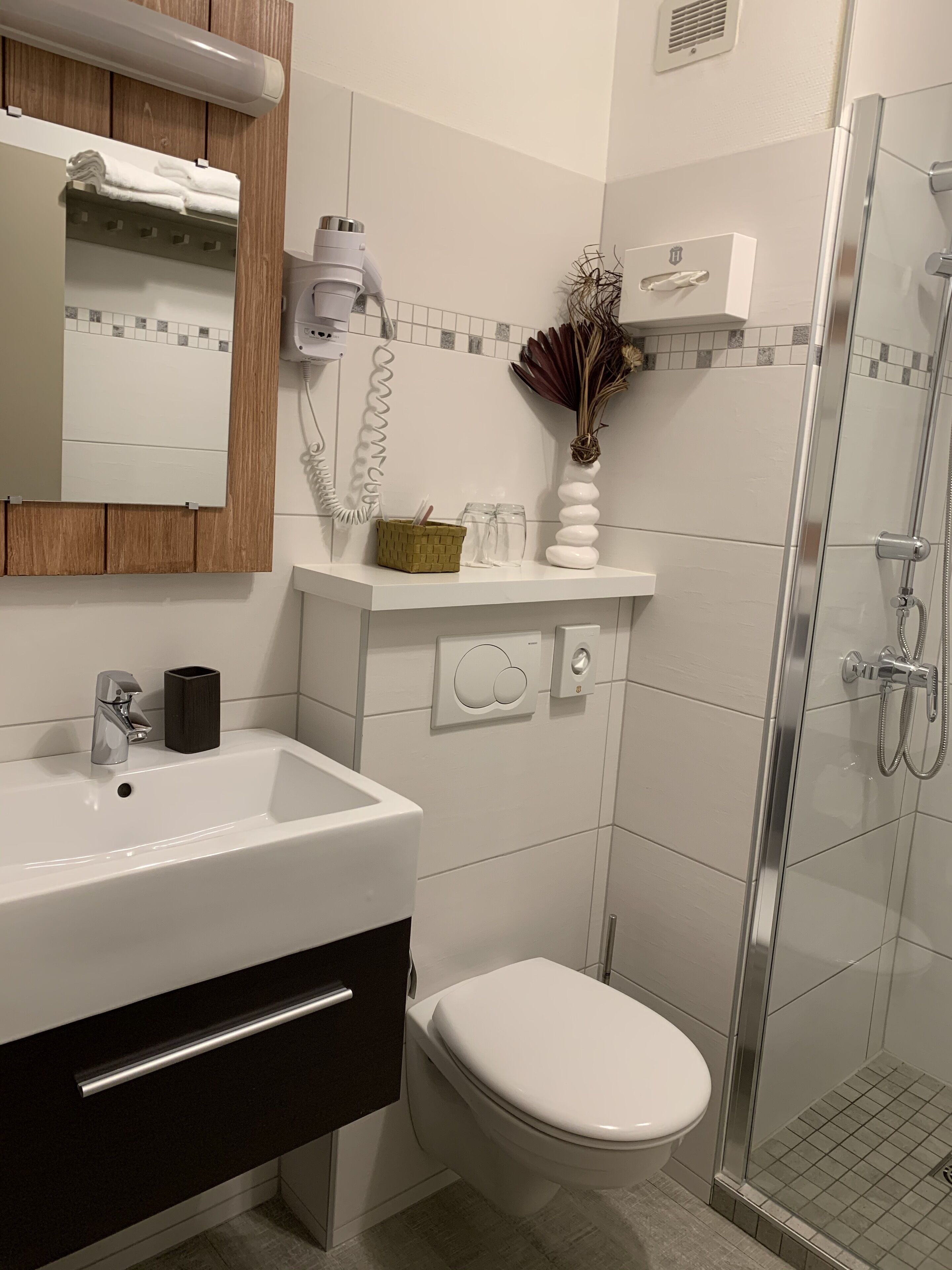 Ein modernes Badezimmer mit Waschbecken, Toilette, Duschkabine aus Glas sowie einem Schminktisch mit Spiegel und Handtuchhalter.